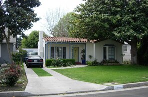 A single-story house with a front yard, a car parked in the driveway, and a small garden. - Jewel West LA Santa Monica (Los Angeles)