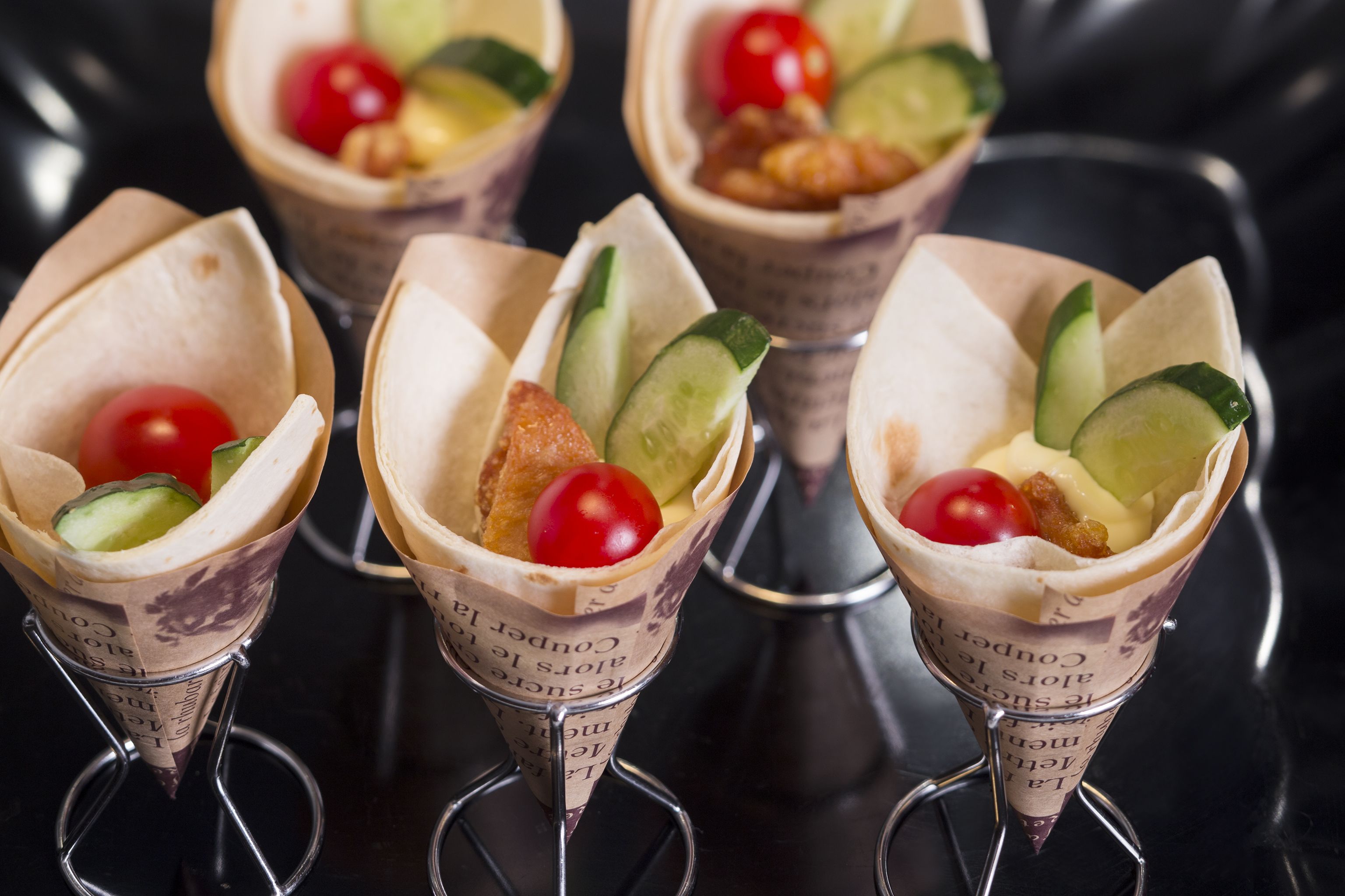 Four food cones with vegetables and a cherry on top.