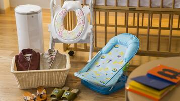 A baby changing station with a changing table, a baby seat, a basket with baby clothes, and a trash can.