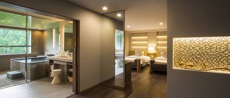 A modern hotel room with a glass shower enclosure, a wooden floor, a bed with a nightstand, and a decorative wall panel.