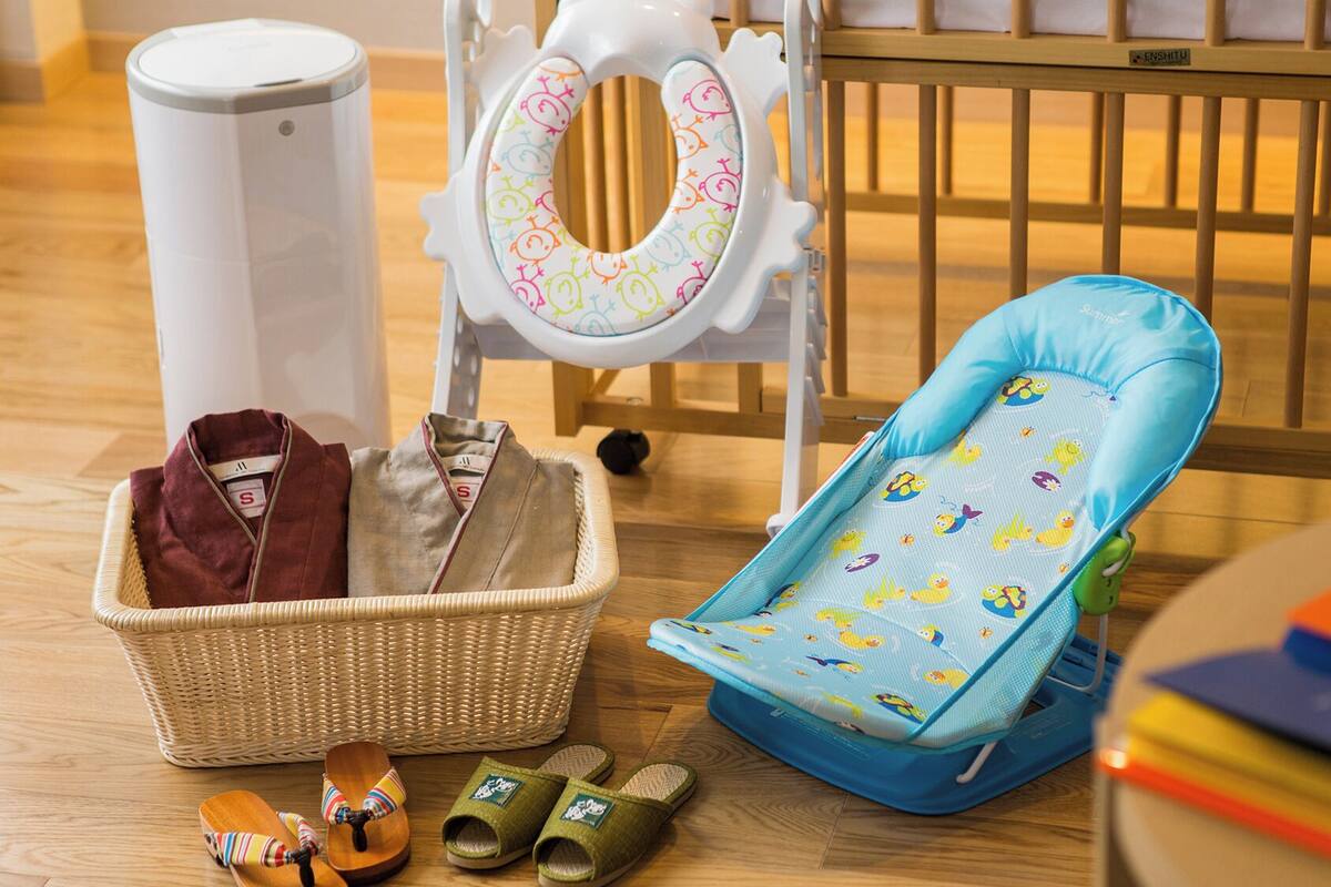 A crib, a changing table, a baby bath, a baby seat, a basket with clothes, and a pair of slippers.