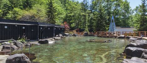Una piscina cristalina rodeada de rocas, un puente de madera y una zona boscosa.