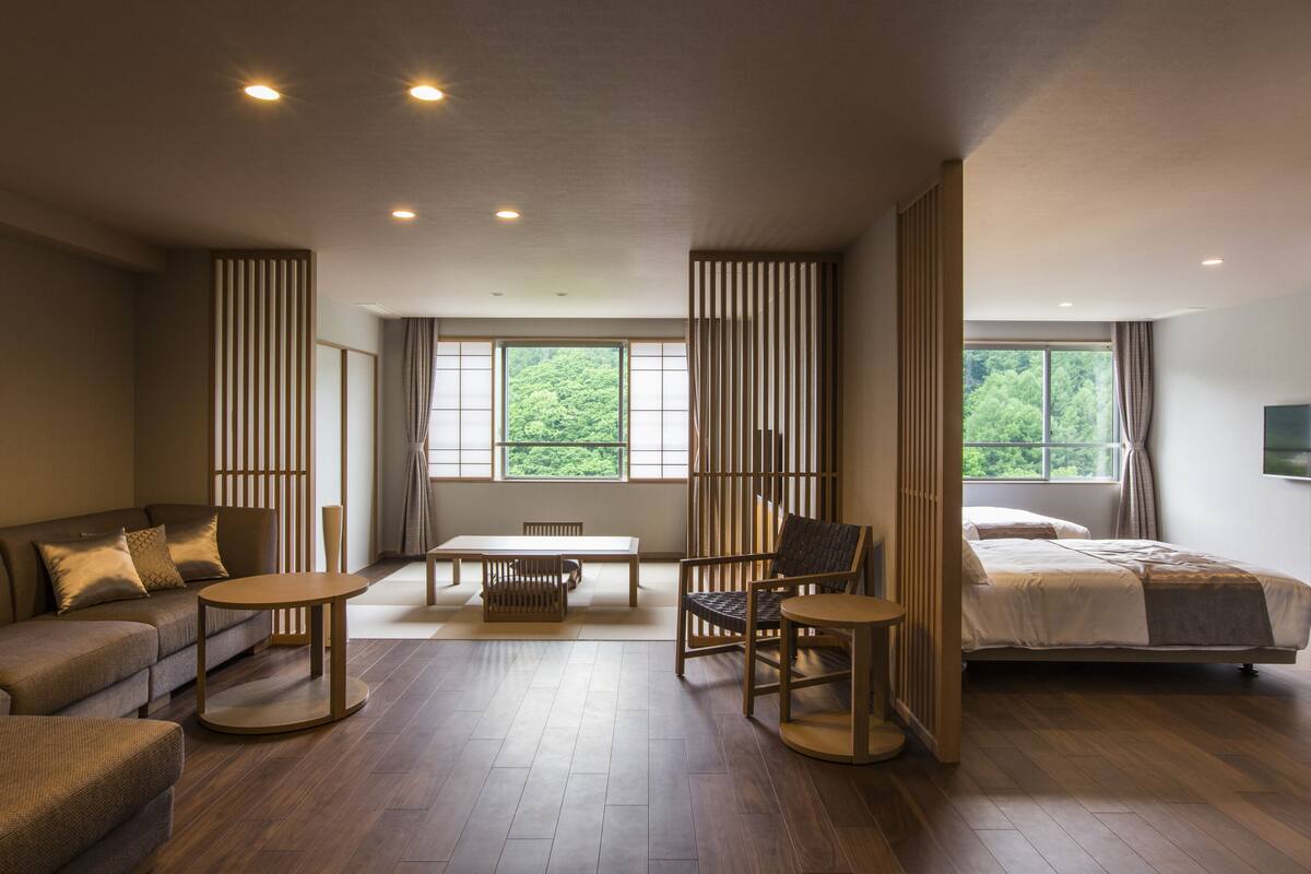A modern hotel room with a sofa, a dining table, a chair, and a bed.