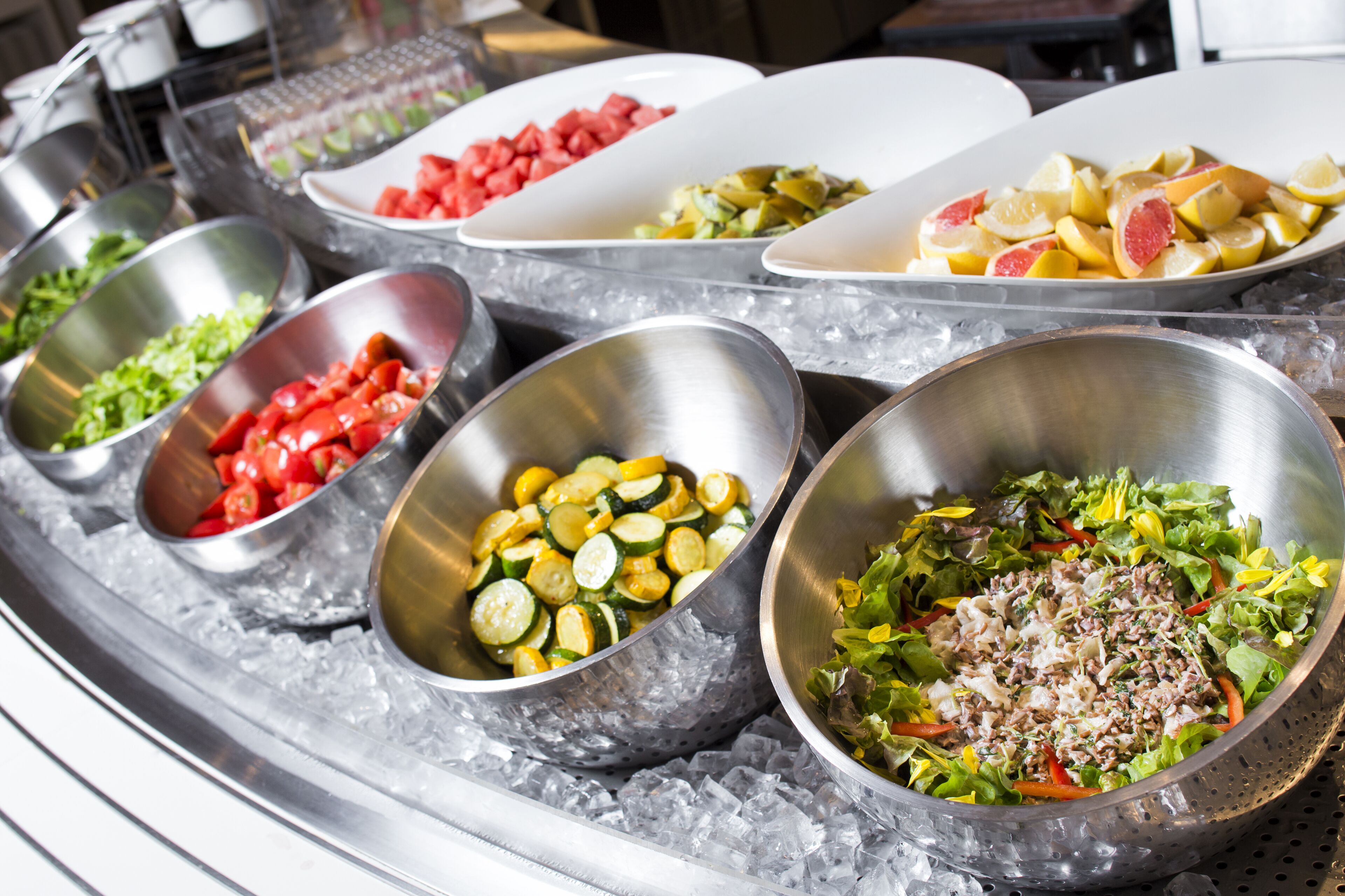 A buffet with various dishes including vegetables, fruits, and salads.