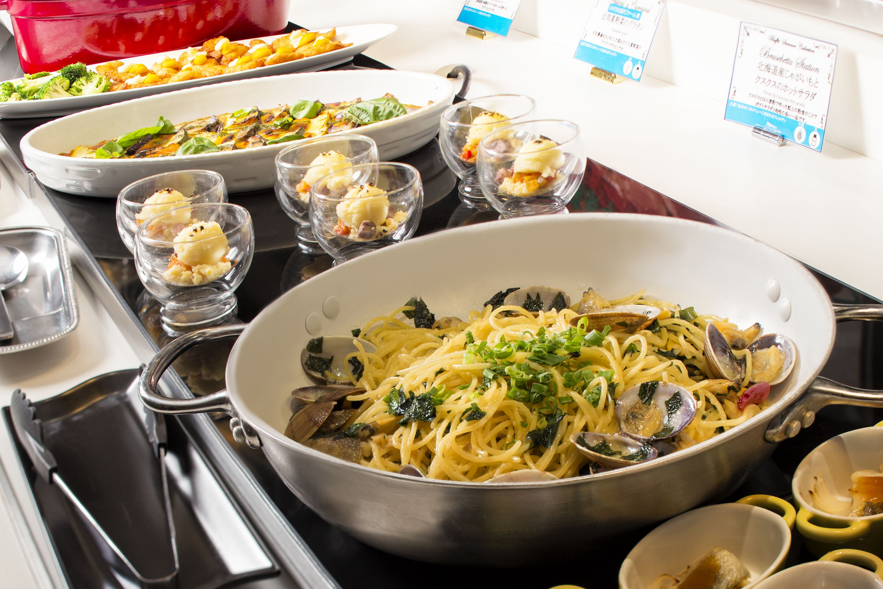 A dining table with various dishes, including pasta and a casserole, and several small glasses.