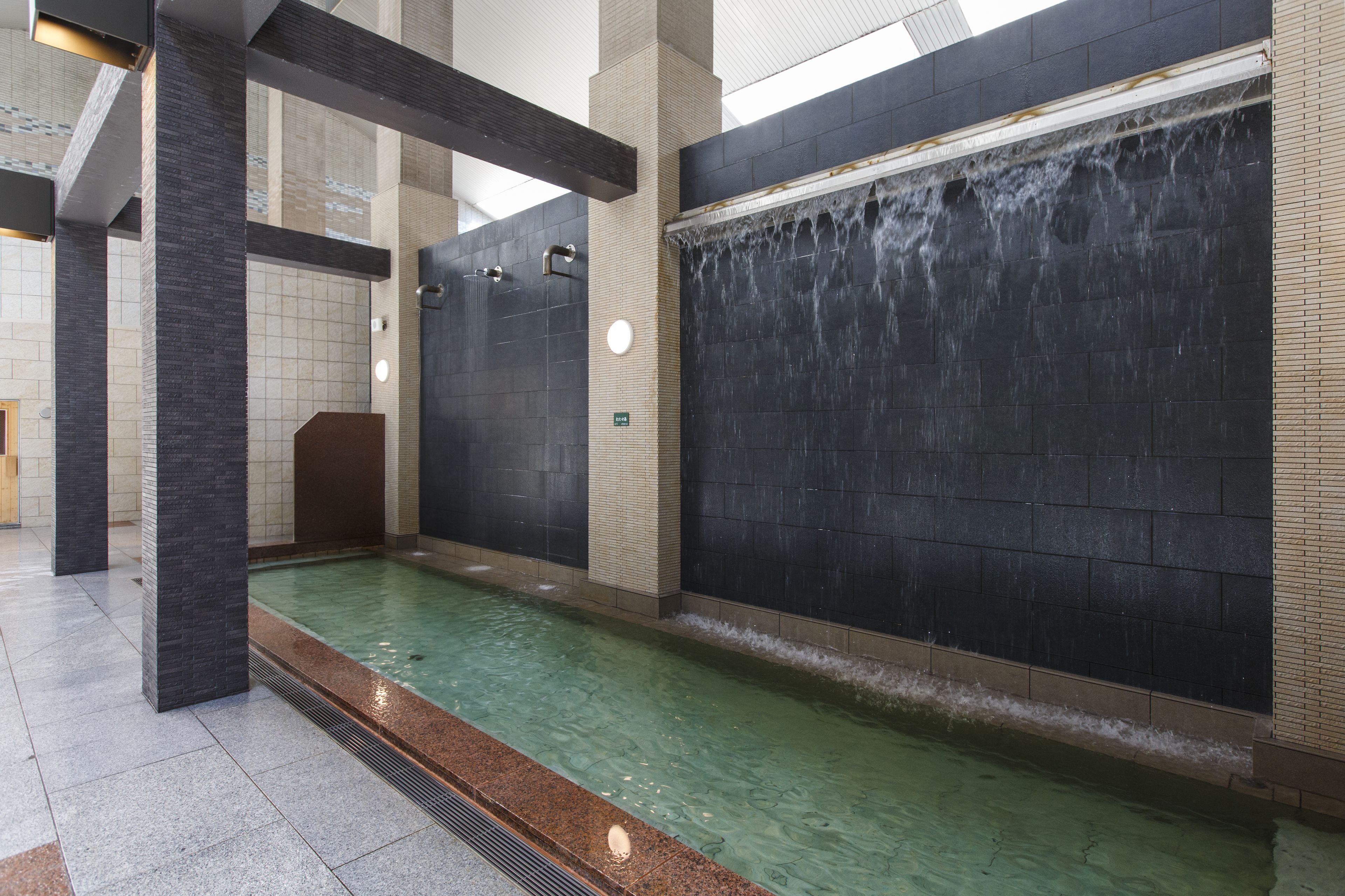 A modern indoor pool area with a water feature, tiled walls, and a clean, well-lit environment.