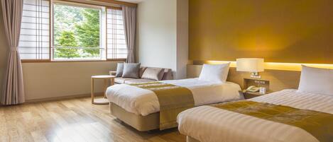 Habitación de hotel con dos camas, una ventana con cortinas, una mesita de noche con lámpara y suelo de madera.