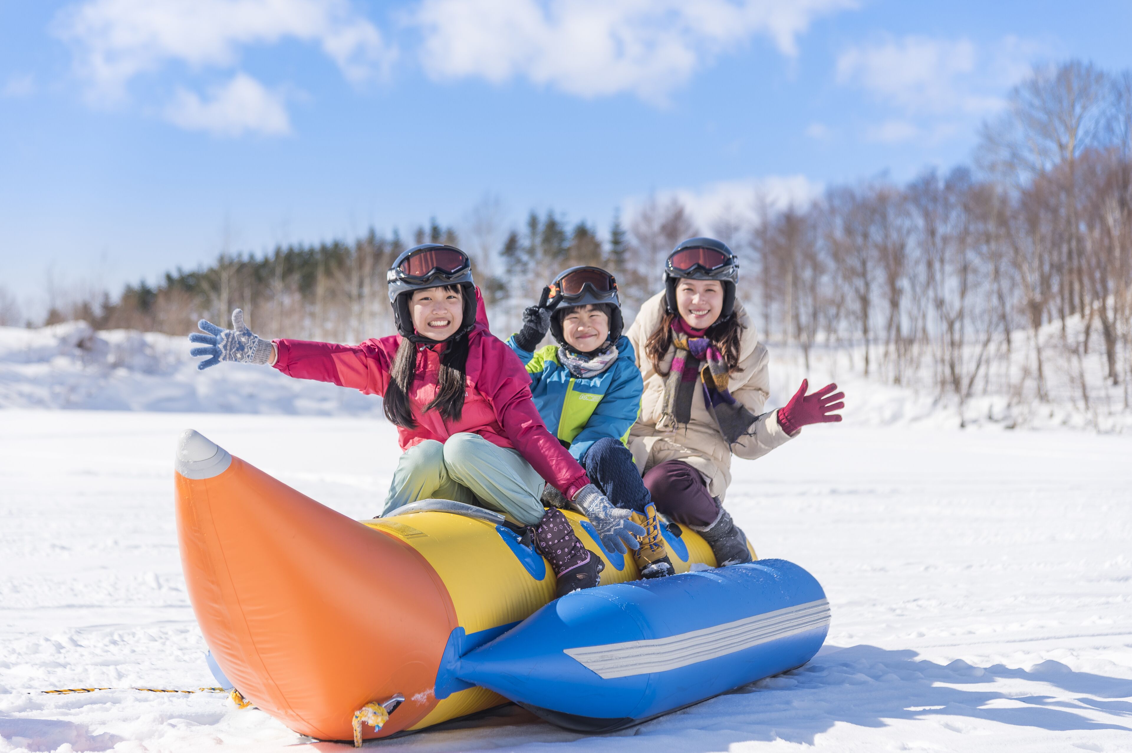 Trois personnes sont assises sur une luge gonflable aux couleurs vives, dans un décor extérieur enneigé.