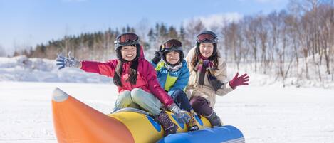 Three people sitting on a colorful inflatable sled in a snowy outdoor setting.