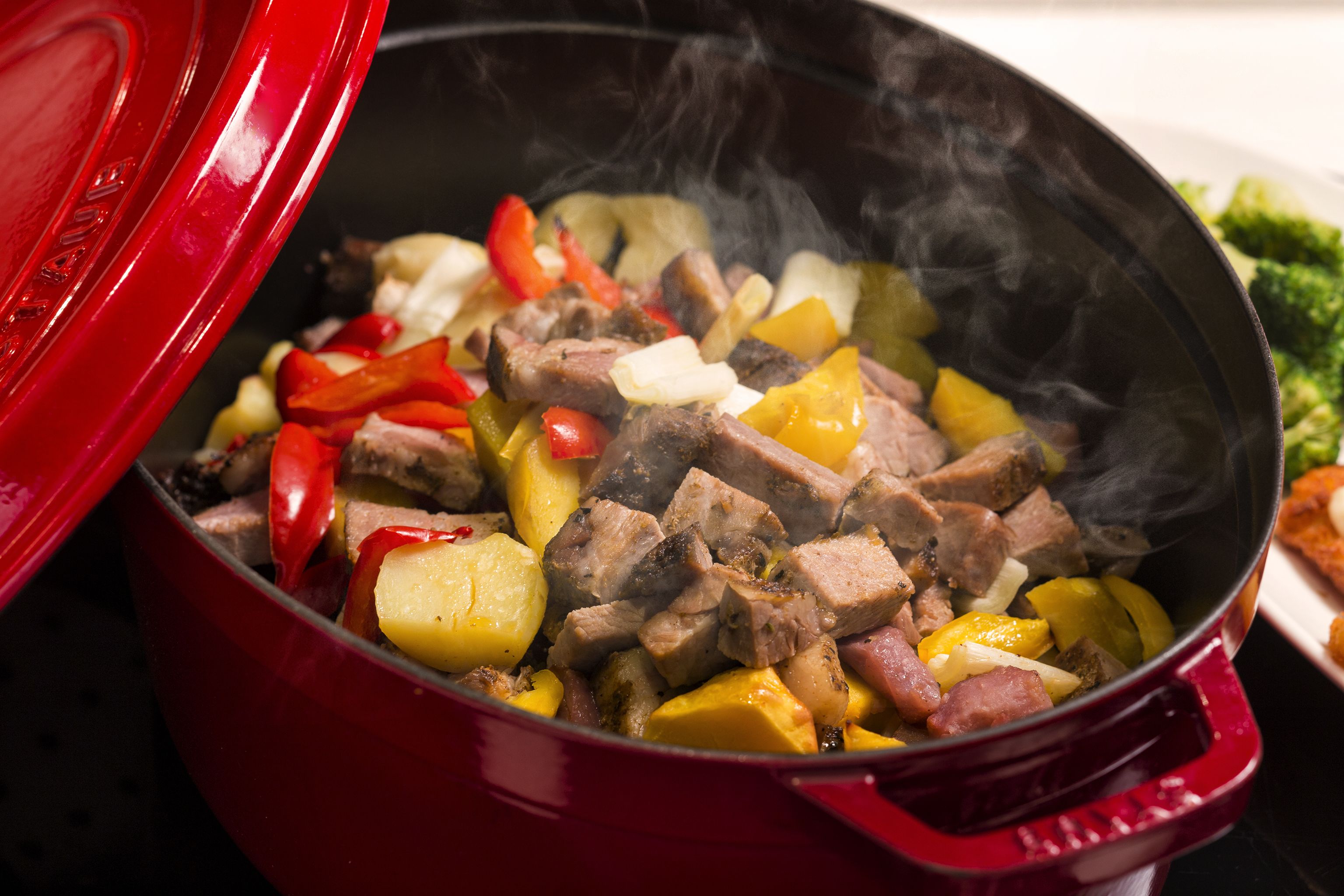 A red pot with a lid, containing a stew with chunks of meat and vegetables.