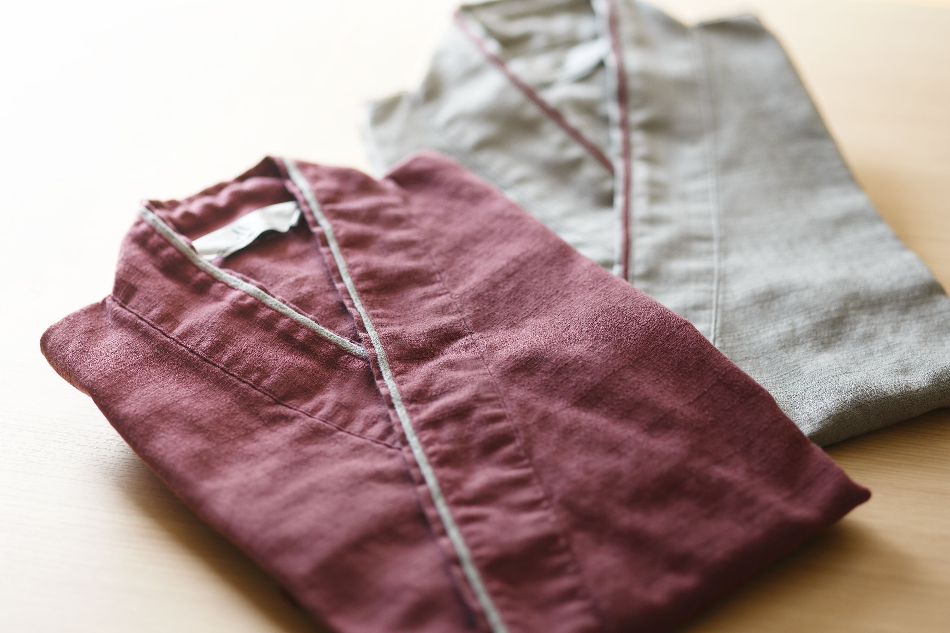 Deux vêtements pliés, l’un d’un rouge foncé et l’autre d’un gris clair, sont posés sur une surface en bois.