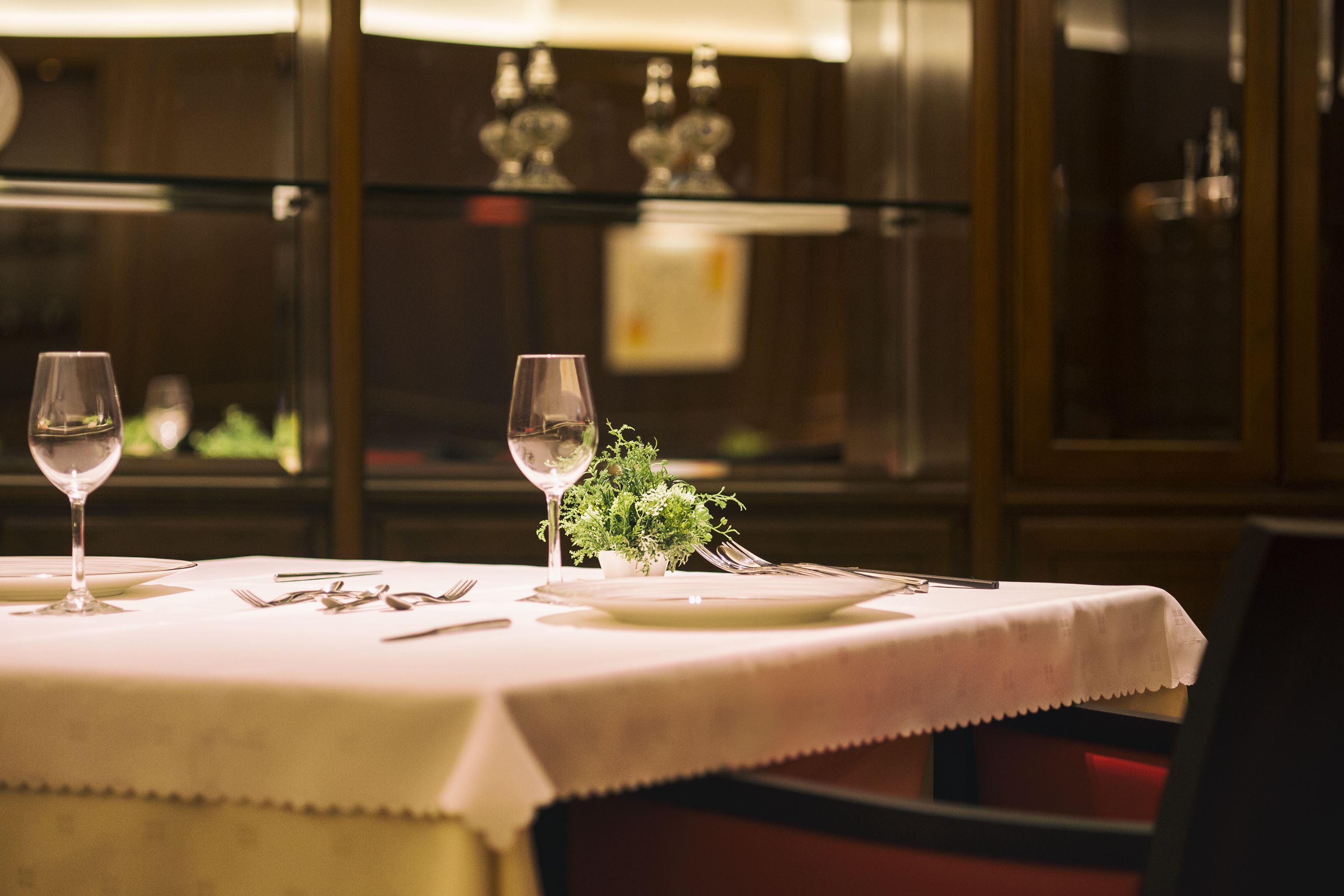 Una mesa de comedor dispuesta con copas de vino, cubiertos y una pequeña planta.