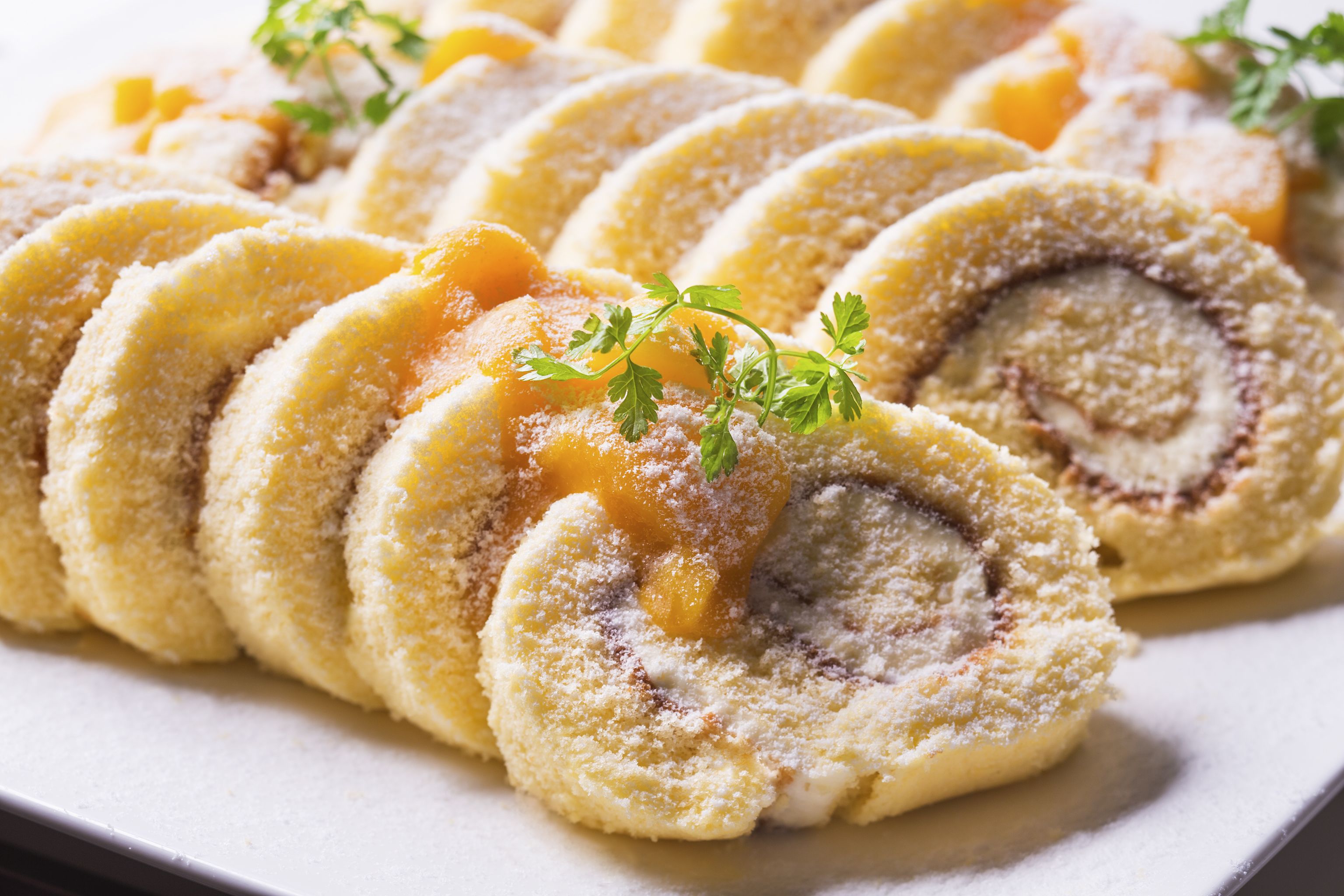 A plate of sliced pastries with a dusting of powdered sugar and a sprig of parsley.