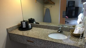 Une salle de bain avec un comptoir en granit, un lavabo, un miroir, un porte-serviettes et un panier rempli de serviettes.