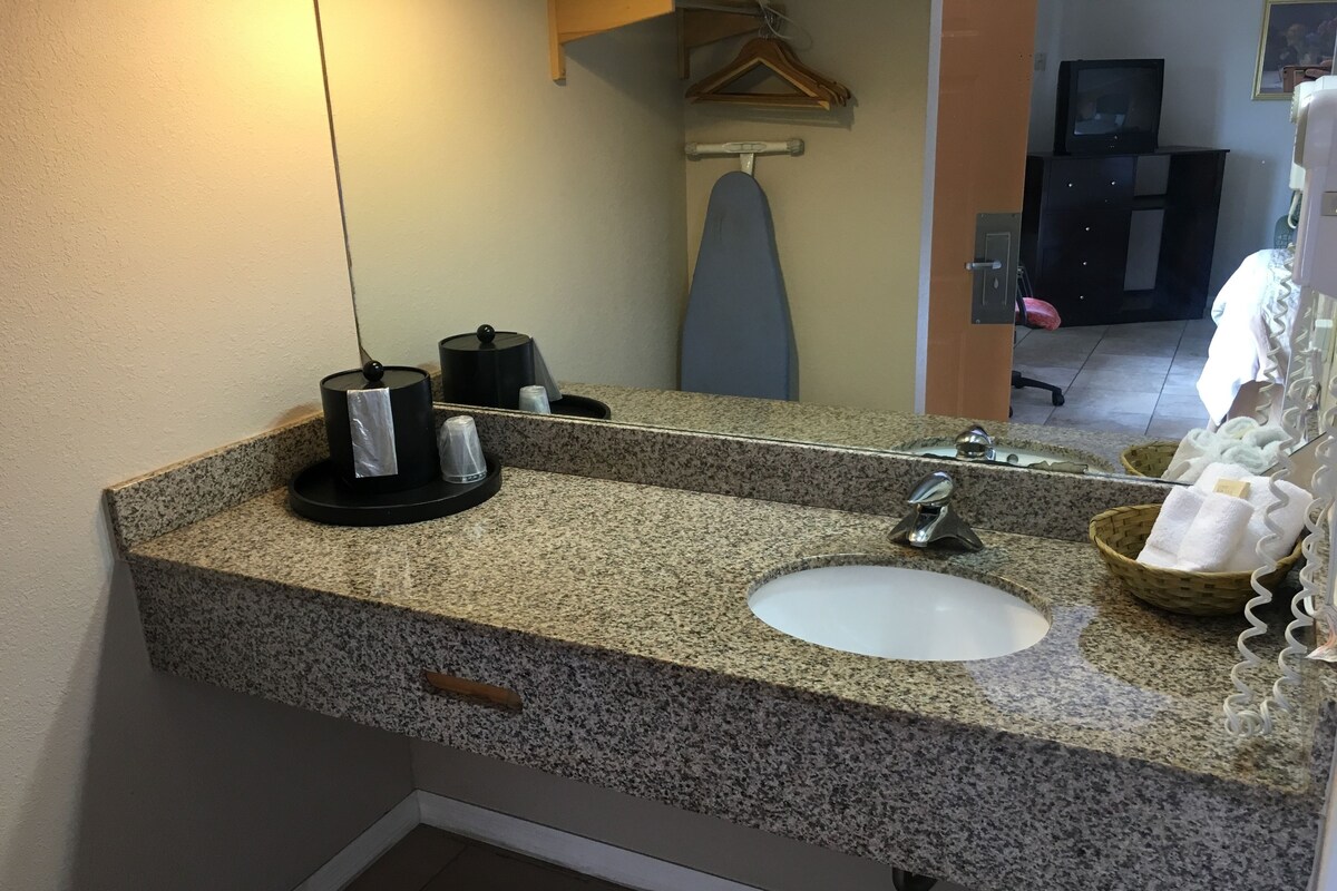A bathroom with a granite countertop, a sink, a mirror, a towel rack, and a basket of towels.