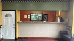 A reception area with a marble counter, framed artwork, and informational signs. - Americas Best Value Inn & Suites North Port (North Port)