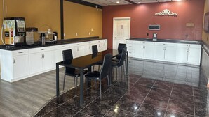 A modern kitchen with a coffee machine, a refrigerator, and a microwave. There is a dining table with chairs and a white cabinet with a black countertop. - Americas Best Value Inn & Suites North Port (North Port)