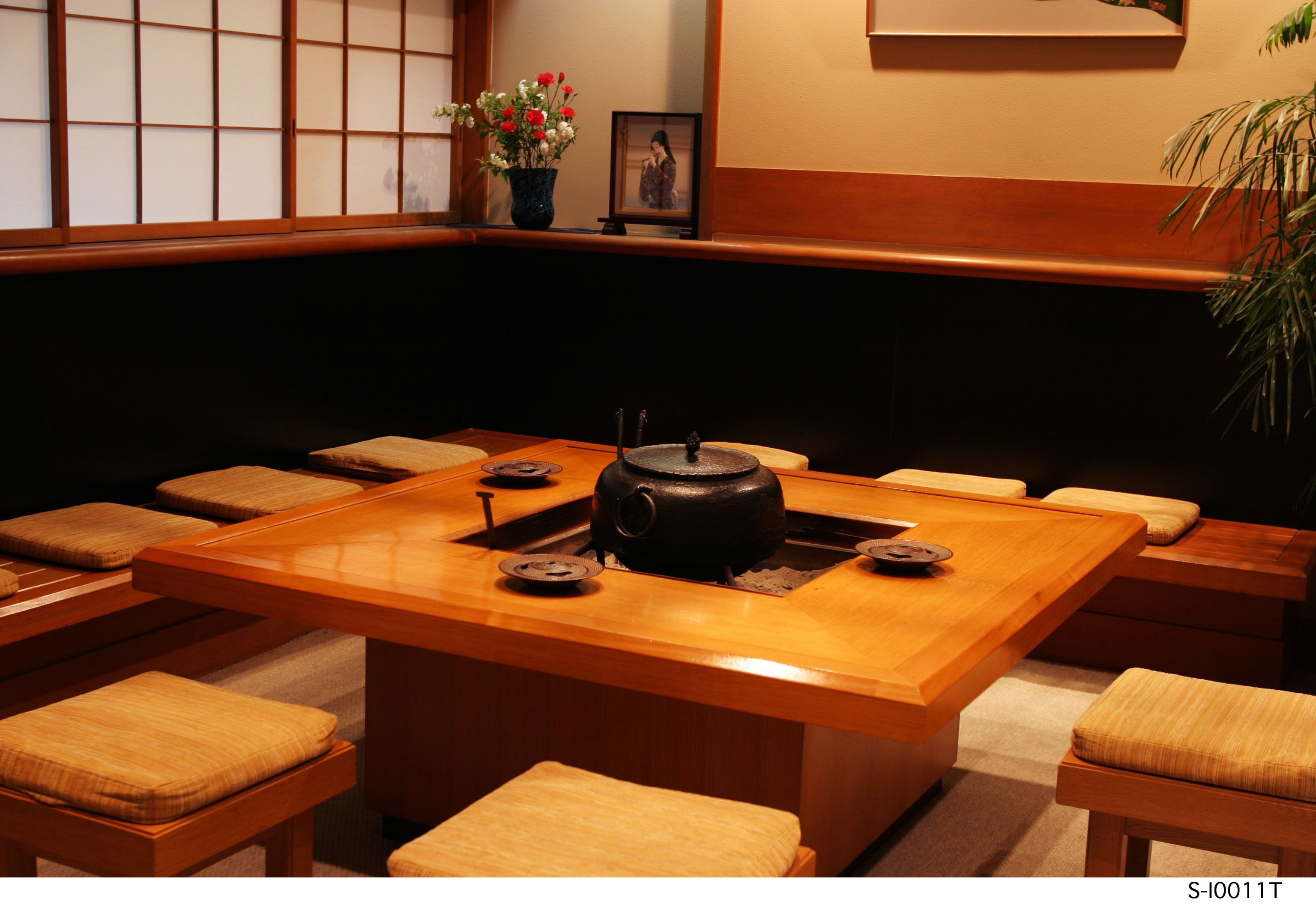Une pièce de style japonais traditionnel, avec des tatamis au sol, une petite table et une bouilloire noire, ainsi qu’un tableau encadré accroché au mur.