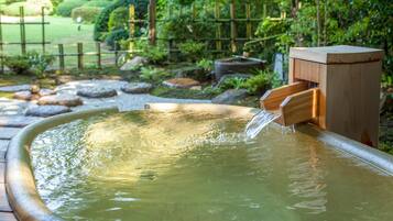 A wooden water feature with a wooden structure and a small waterfall, surrounded by rocks and greenery.