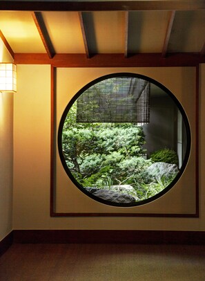 Une fenêtre circulaire donnant sur un jardin, un luminaire fixé au mur et une structure de plafond en bois.