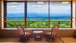A room with a large window offering a view of a mountainous landscape. There are two wicker chairs and a small round table in the room. - Nasu Onsen Sanraku (Nasu)