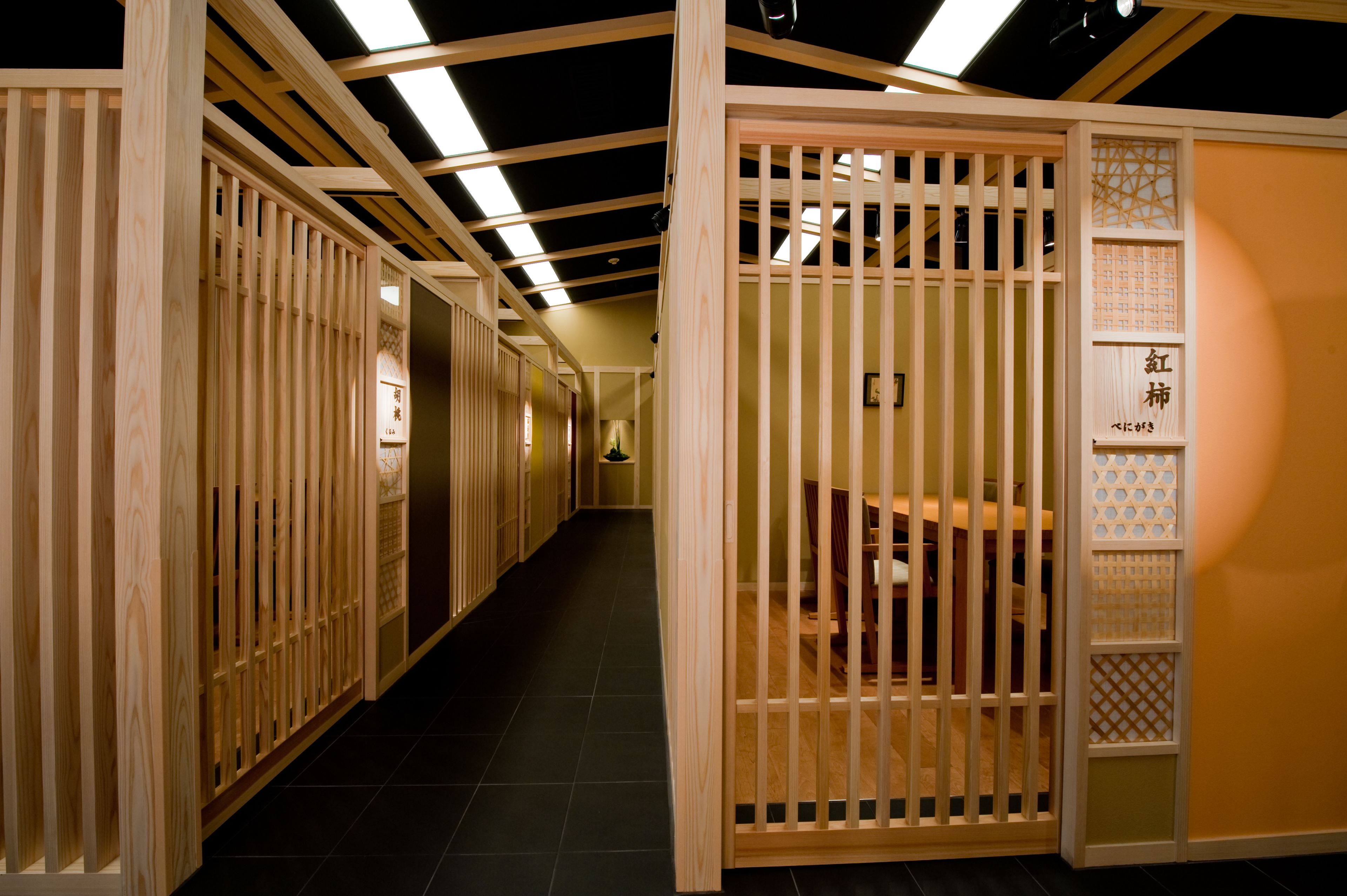 A corridor with wooden partitions and a tiled floor, leading to a seating area with a table and chairs.