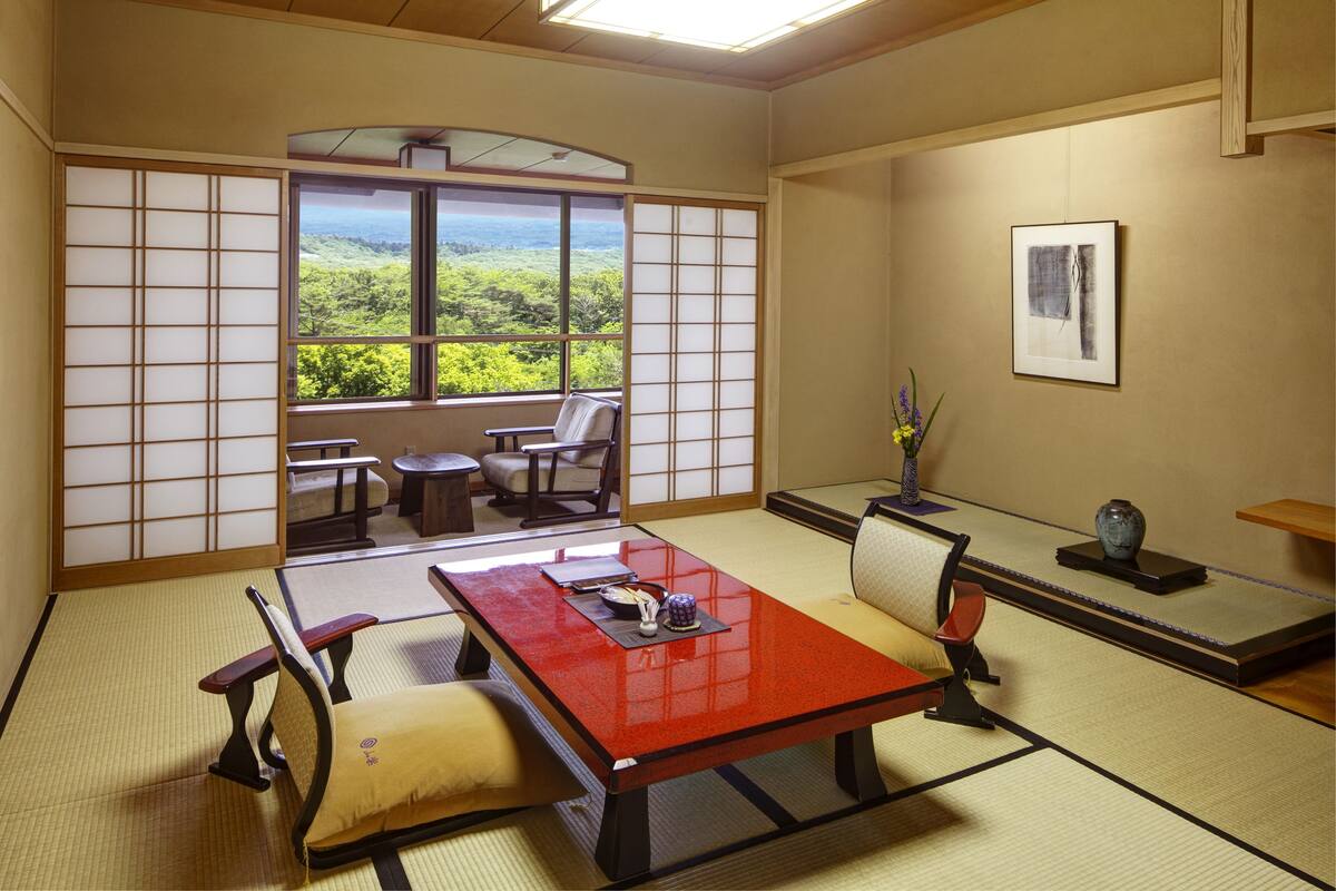 A traditional Japanese room with tatami flooring, a low table, and a view of a lush landscape through a shoji screen.