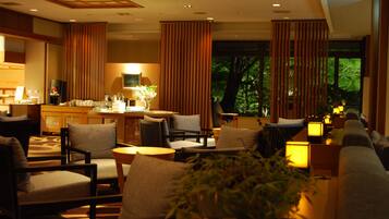 A hotel lobby with a seating area, a reception desk, and large windows with a view of trees.