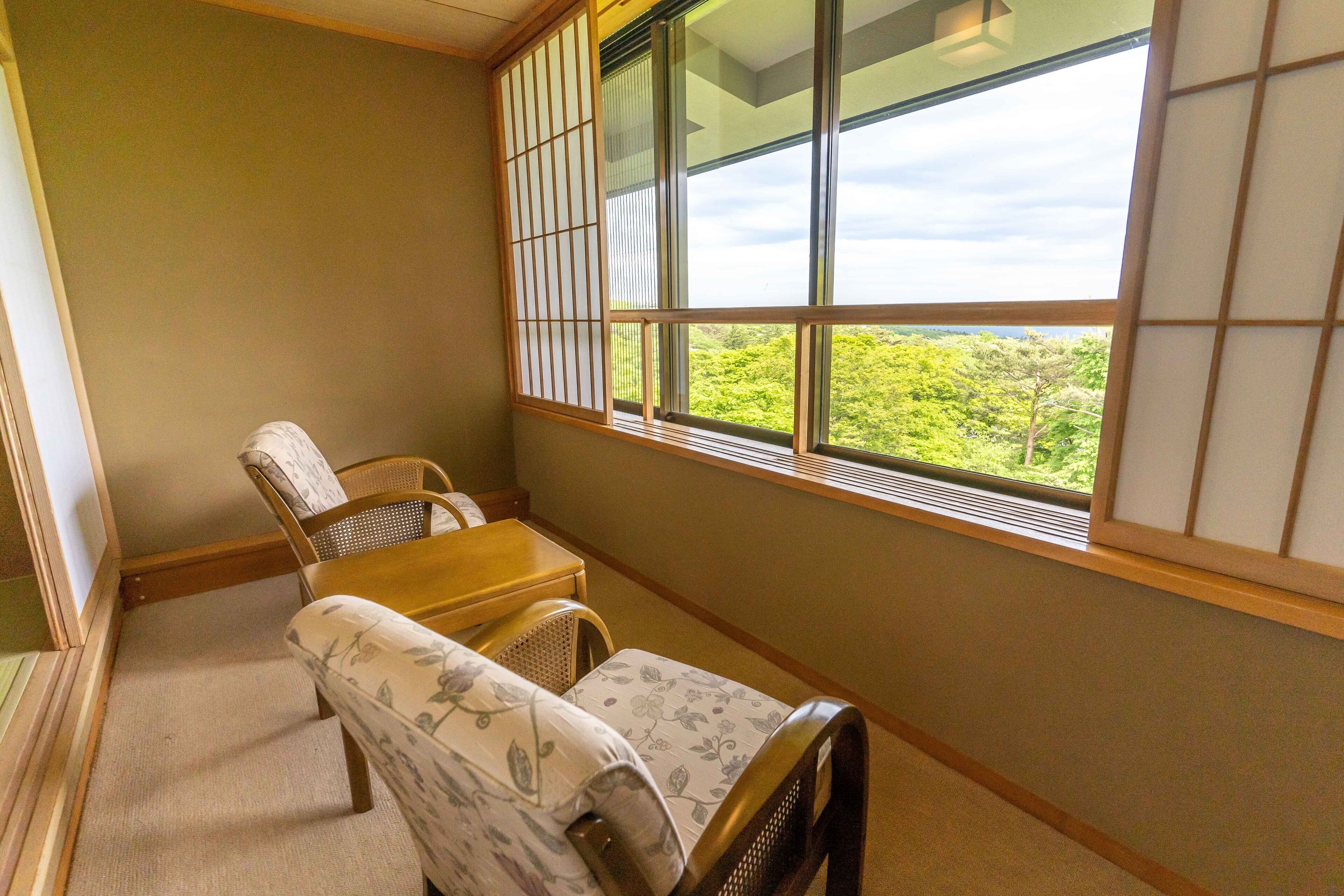 A traditional Japanese room with tatami flooring, a low wooden table, two tatami mats with cushions, and a large window with shoji screens.