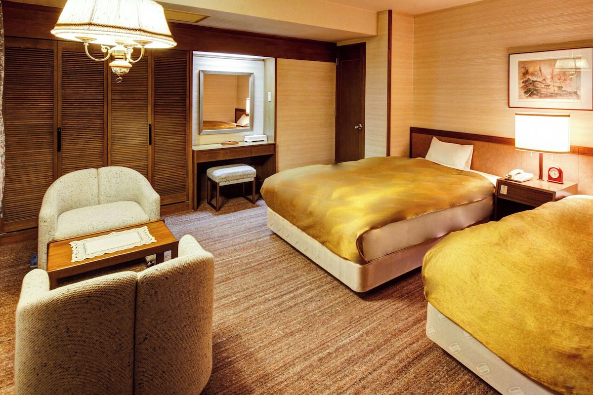 A hotel room with two beds, a desk, a chair, a mirror, and a lamp.