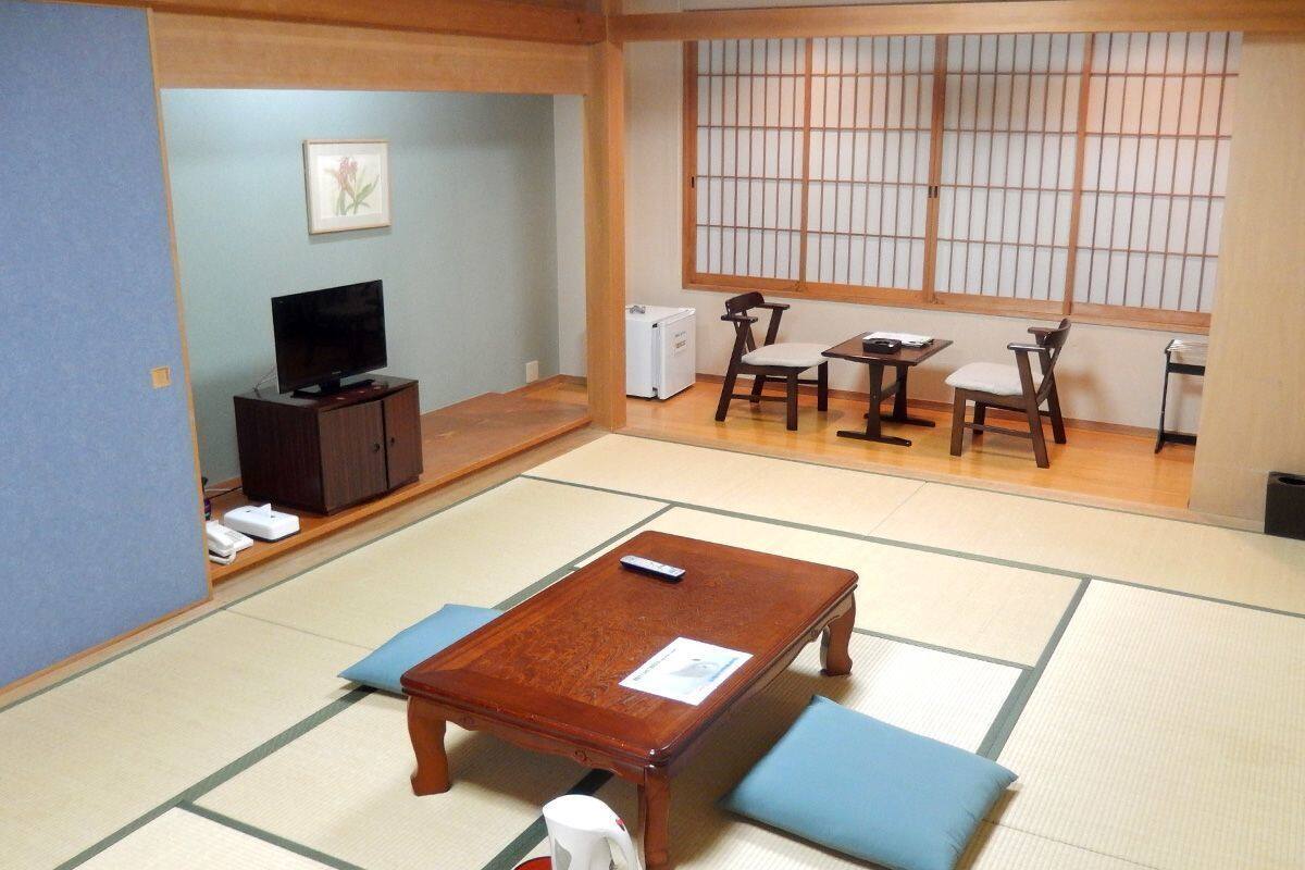 A traditional Japanese-style room with tatami flooring, a low wooden table, a television, and a shoji screen.