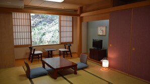 A traditional Japanese room with tatami flooring, a low table, chairs, a television, and a sliding door.