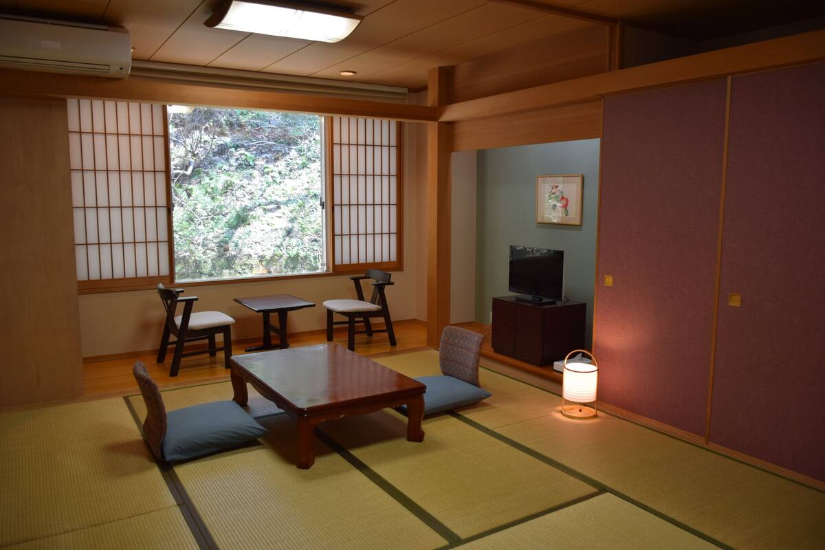 A traditional Japanese room with tatami flooring, a low table, chairs, a television, and a sliding door.