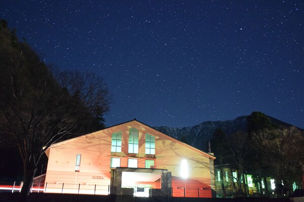 A building with a sloped roof and multiple windows, surrounded by trees and mountains under a starry night sky. - Hotel Daisen Shirogane (Daisen)