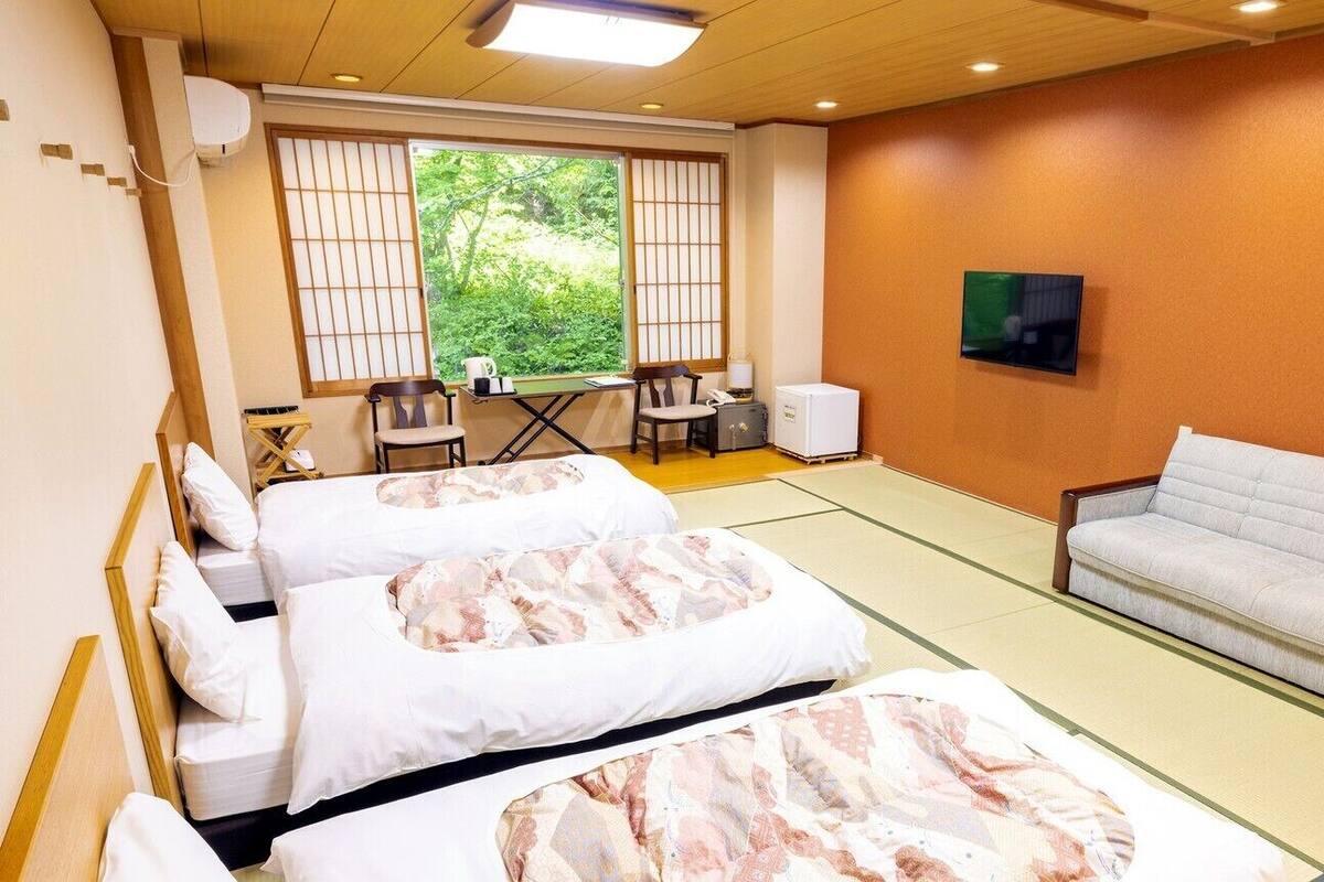A hotel room with two beds, a sofa, a TV, and a view of greenery through the window.