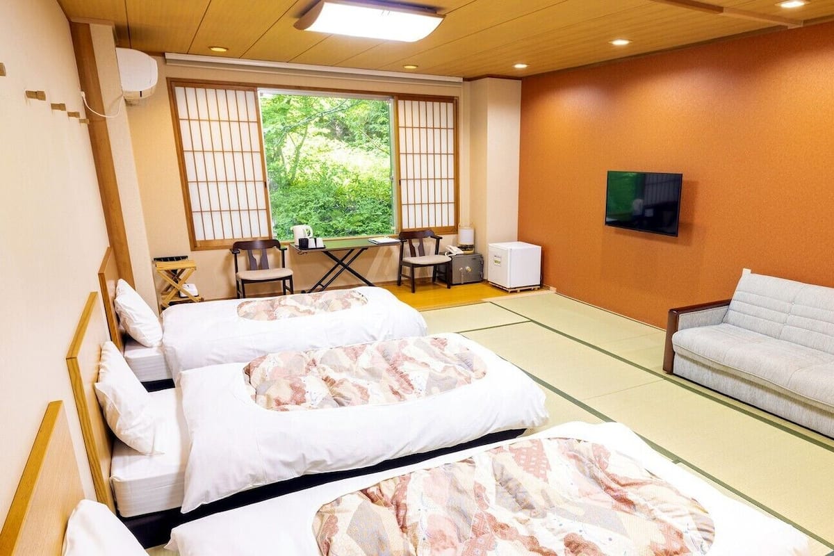Habitación de hotel con dos camas, un sofá, un televisor y vistas a zonas verdes por la ventana.