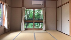 A traditional Japanese room with tatami flooring, sliding doors, and a view of greenery outside.