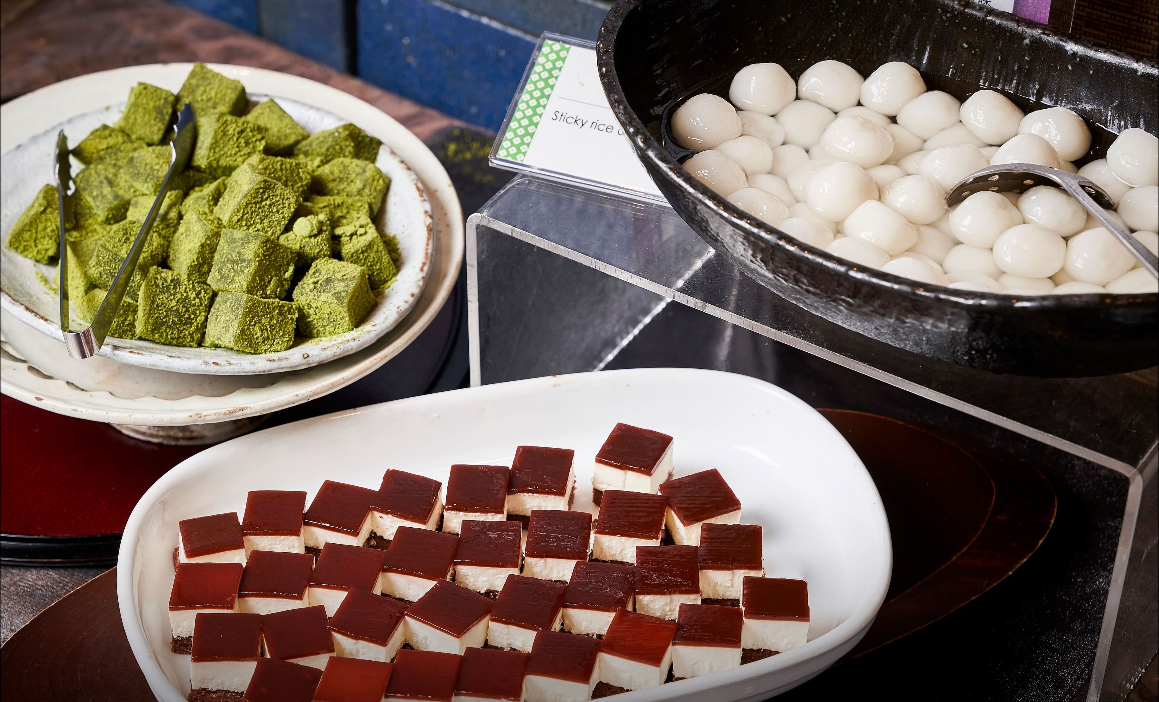 A variety of food items including sticky rice, green cubes, and layered desserts.
