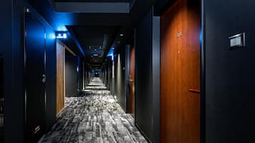 A hotel corridor with a carpeted floor, wooden doors, and a blue-lit exit sign.