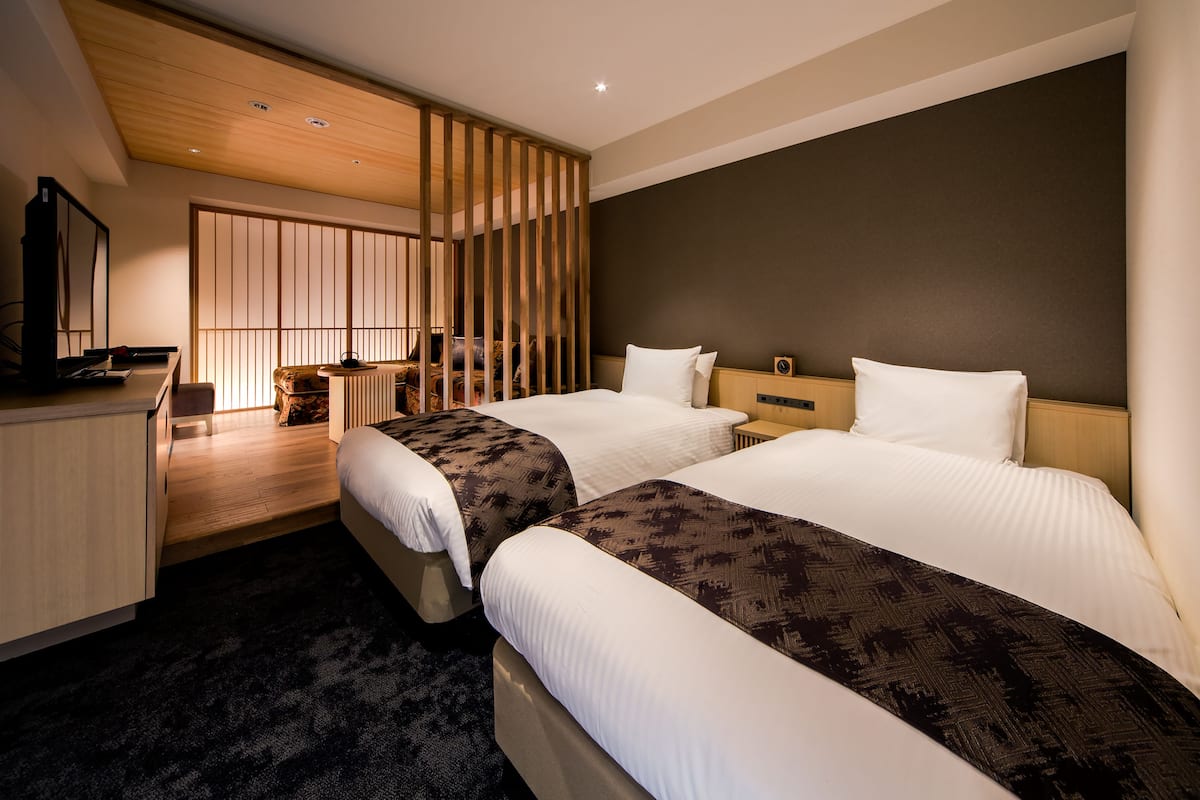Ein Hotelzimmer mit zwei Betten, einem Schreibtisch, einem Sessel und einem Fernseher.