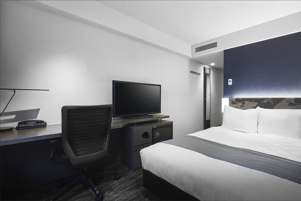 Ein Hotelzimmer mit Bett, Schreibtisch mit Computer, Stuhl, Fernseher und Kleiderschrank.