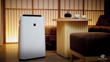 Una habitación moderna con un purificador de aire blanco, una pequeña mesa de madera con una tetera negra, dos cuencos blancos y un sofá marrón.