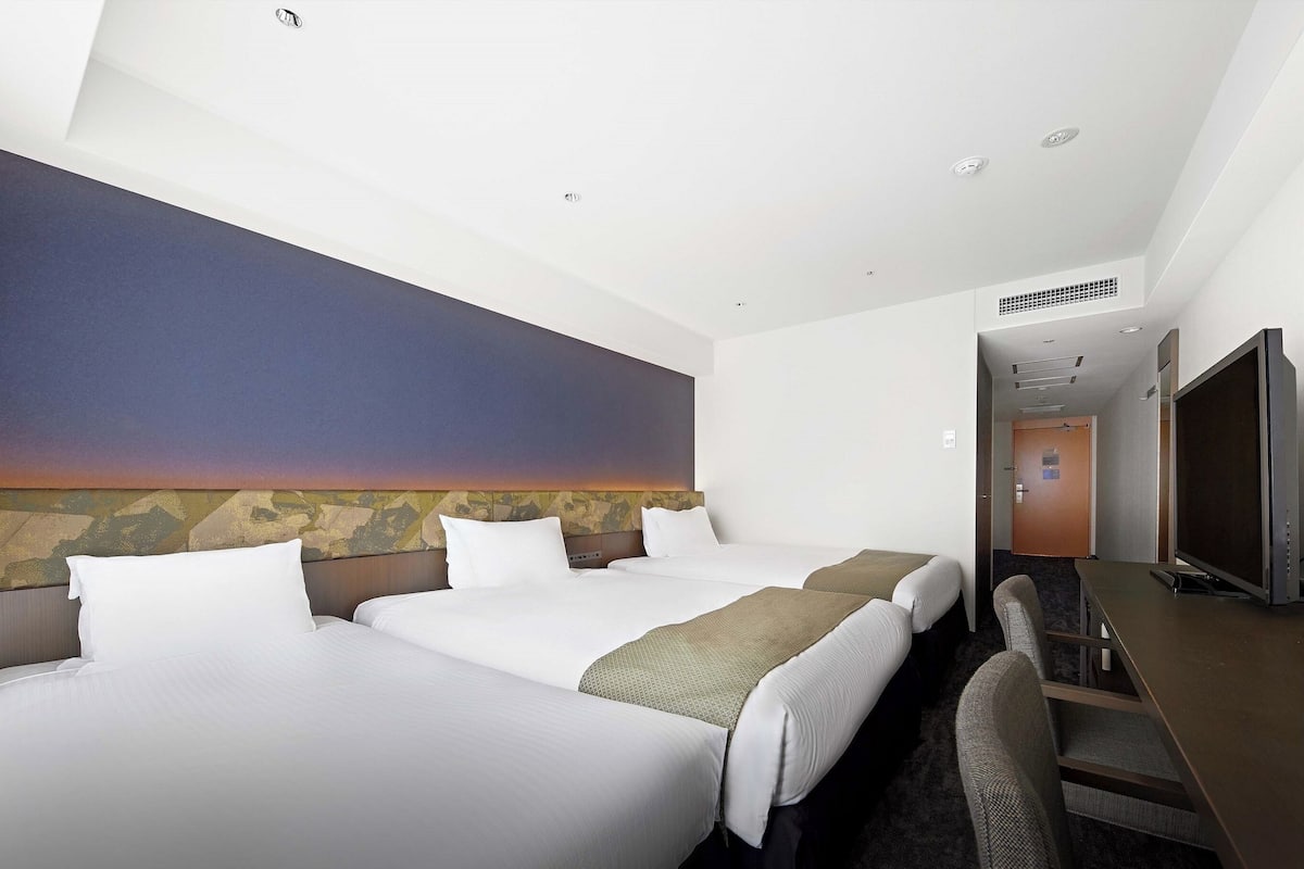 Ein Hotelzimmer mit zwei Betten, einem Schreibtisch, einem Fernseher und Blick auf den Sonnenuntergang.