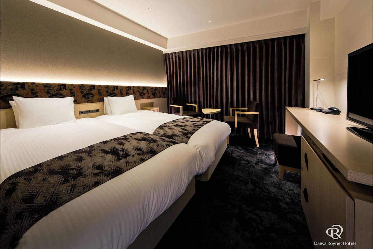 Ein Hotelzimmer mit einem großen Bett, einem Schreibtisch mit Computer, einem Stuhl und einem Fernseher.