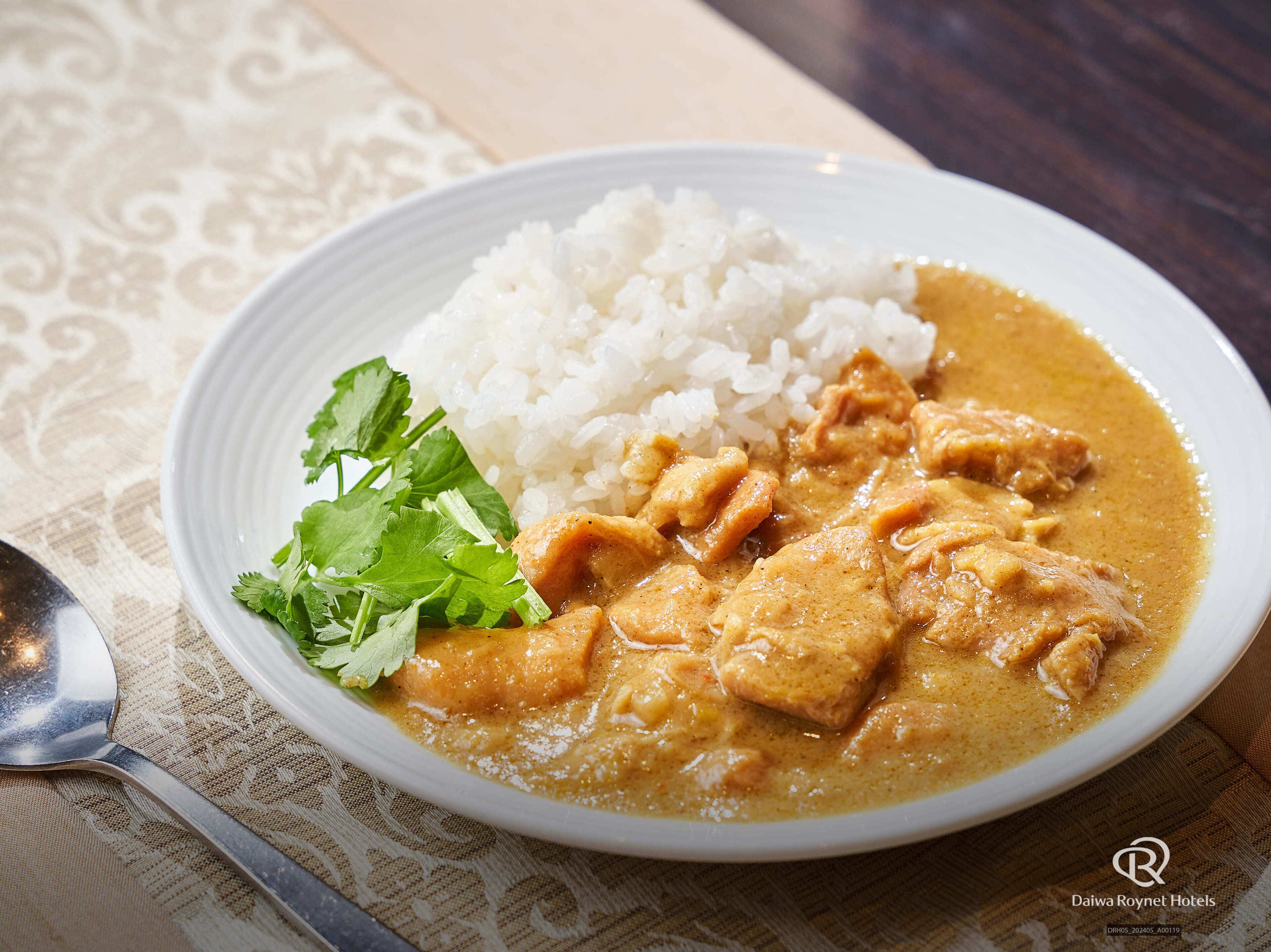A plate of chicken curry with rice and a garnish of cilantro.