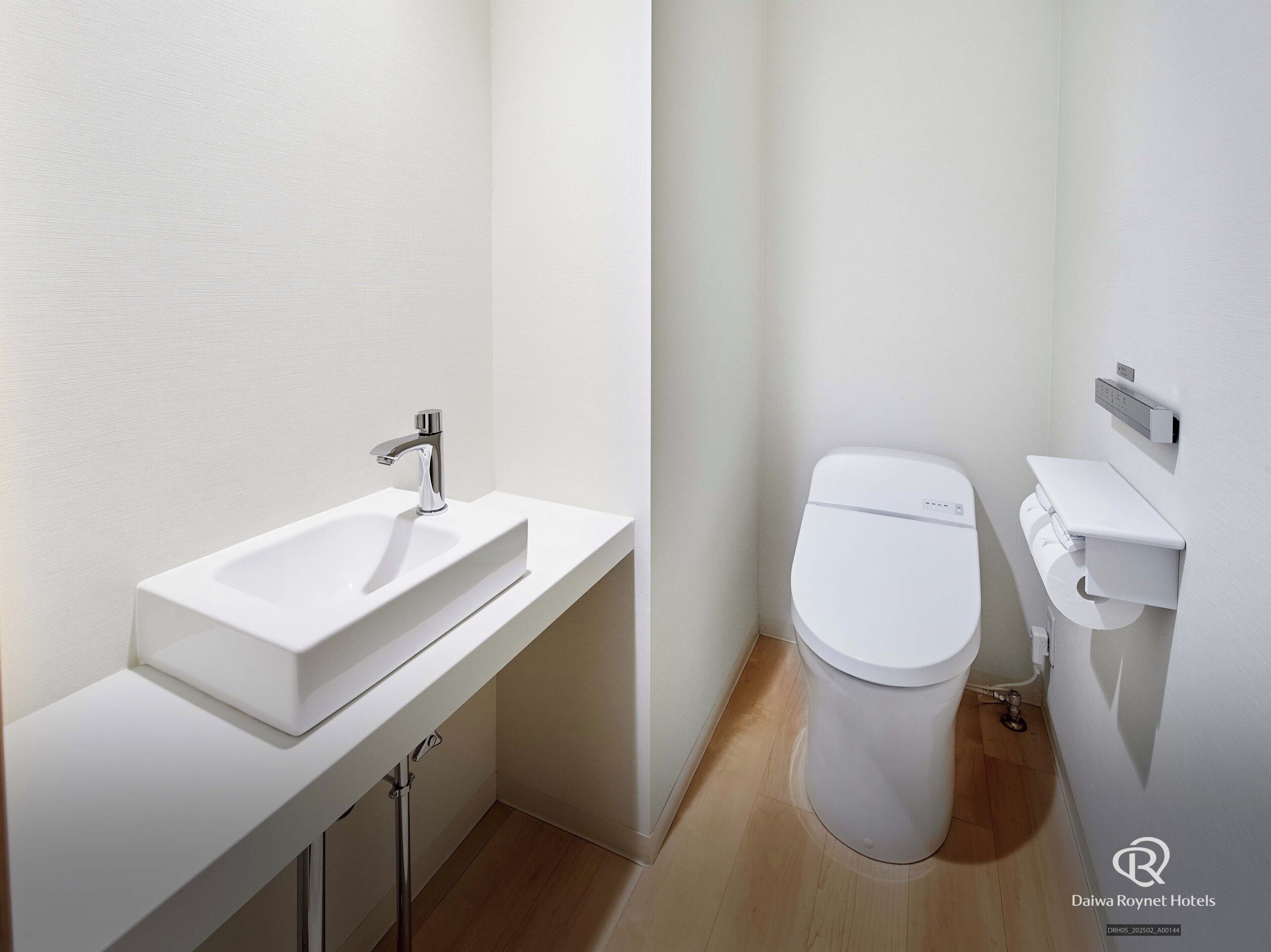 A modern bathroom with a white sink, chrome faucet, and toilet.