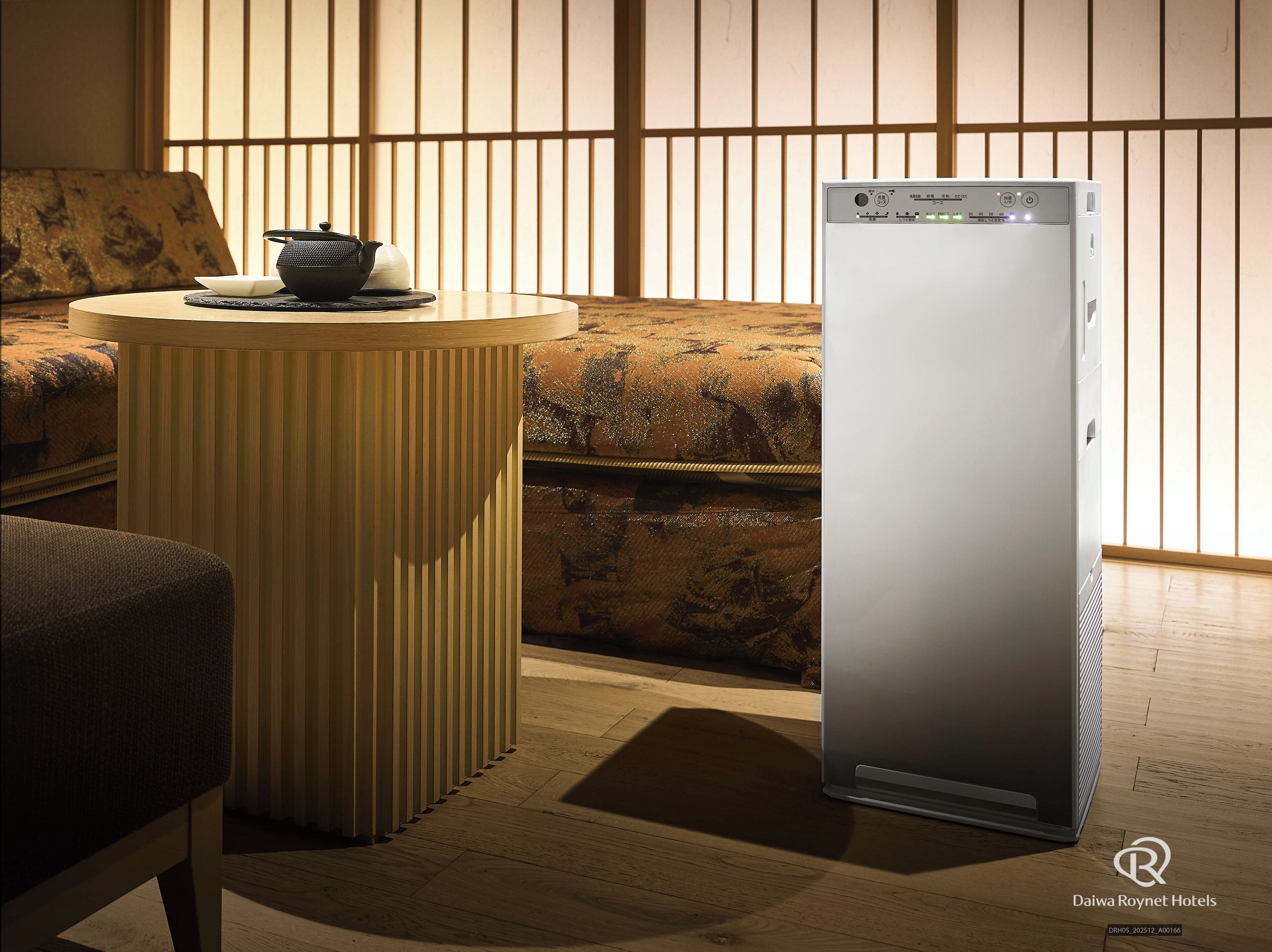 A modern hotel room with a traditional Japanese-style sofa, a round wooden table with a tea set, and a sleek, contemporary air conditioning unit.