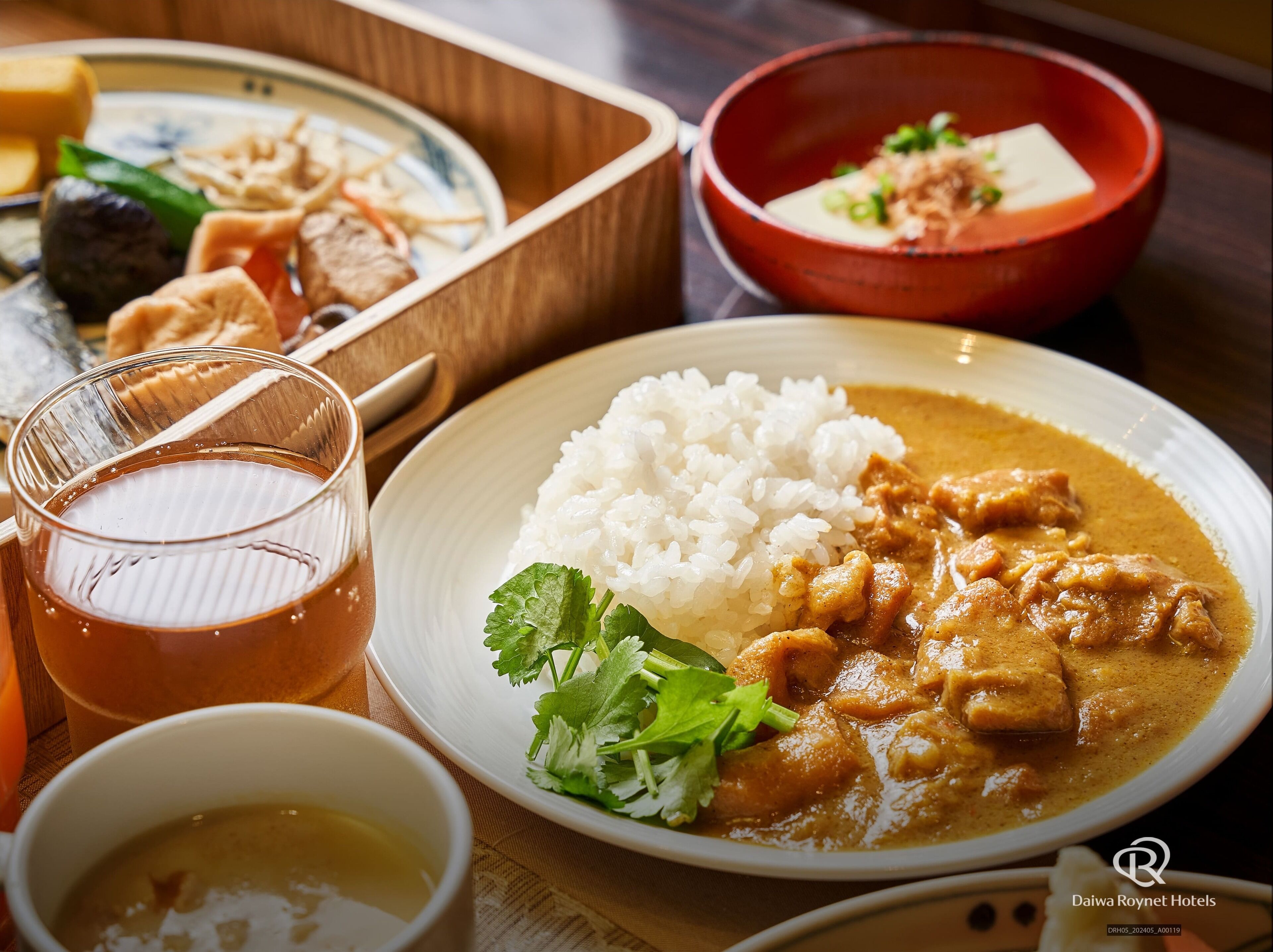 A meal with white rice, curry, and a glass of tea on a wooden table.