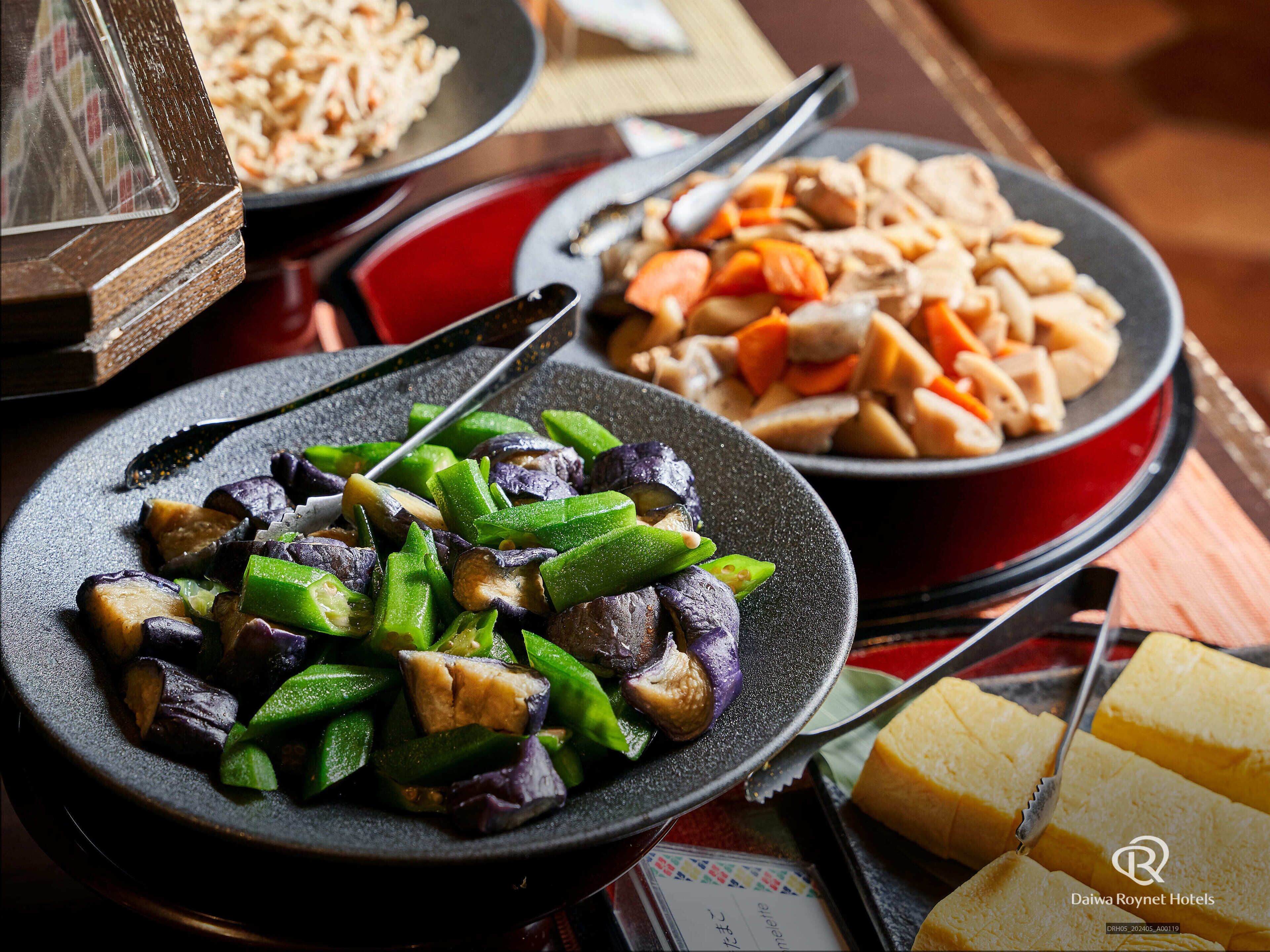 Une table à manger avec différents plats, notamment une assiette de légumes sautés, un bol de riz et une assiette de poulet.