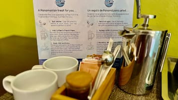 A coffee-making setup with a French press, two cups, and a wooden box with coffee beans. Instructions for making coffee are visible on a sign.